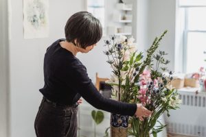 A woman carefully arranges a vibrant floral display in a well-lit home setting. — Over Skirting Boards Provide Quick Updates
