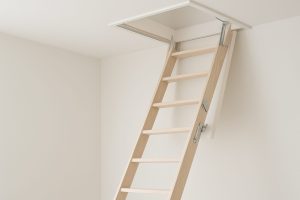 A wooden loft ladder leading up into a ceiling opening, showcasing a modern interior design
